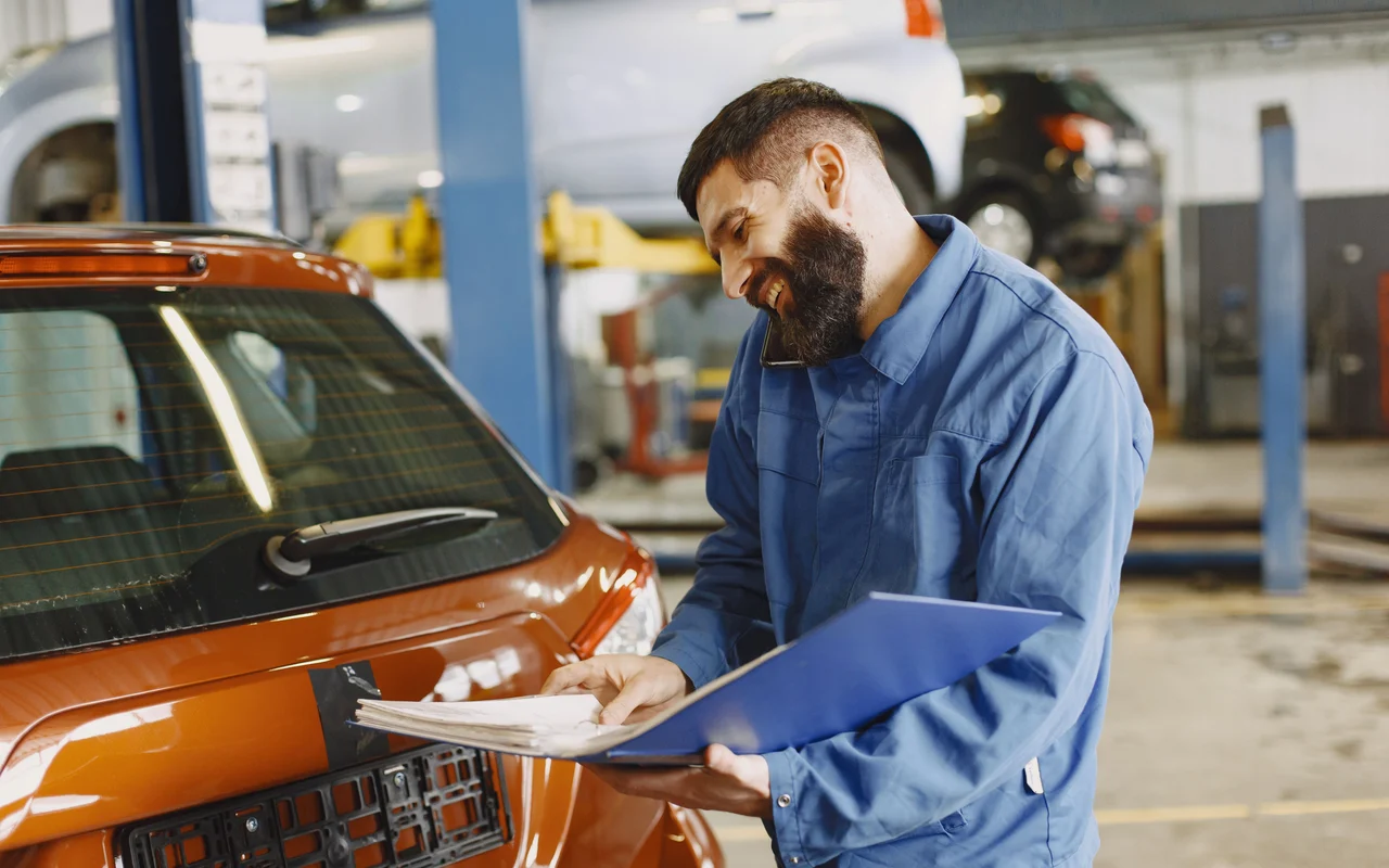 Ein Garagist sieht neben einem Auto ein Dossier durch.